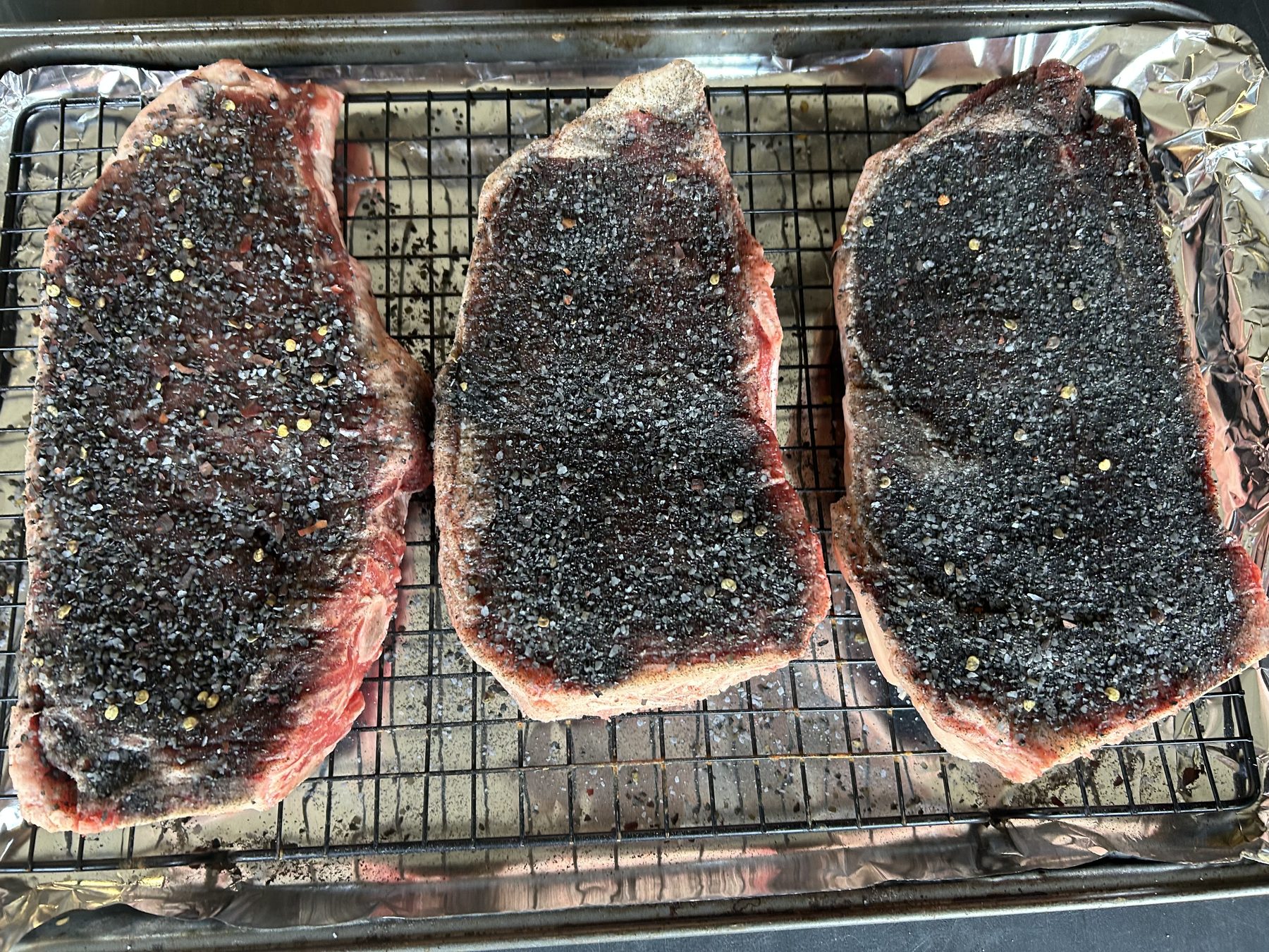 Three steaks coated with Black Heart Steak Seasoning on a wire rack before cooking