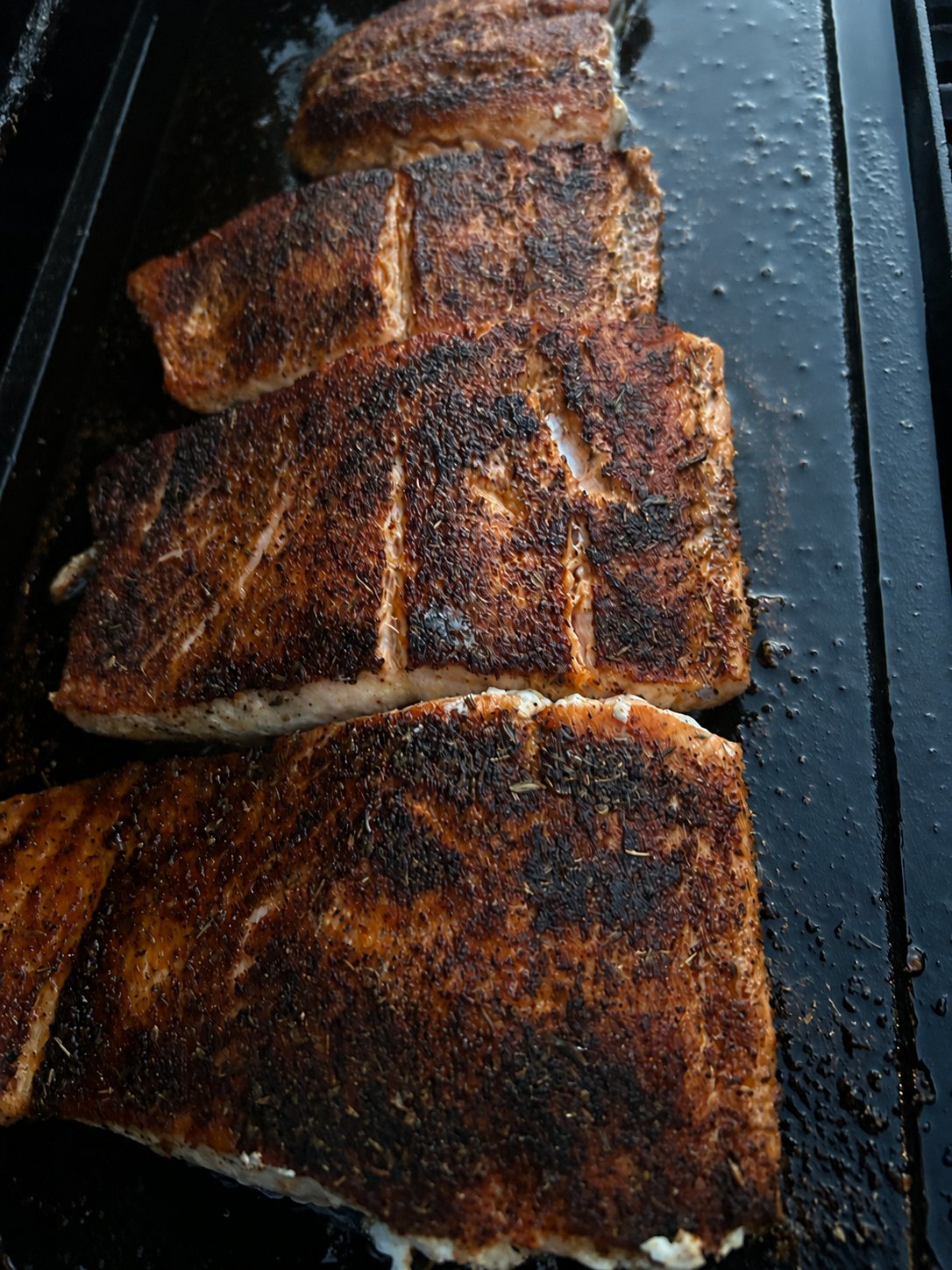 Blackened salmon cooking on a flat top grill