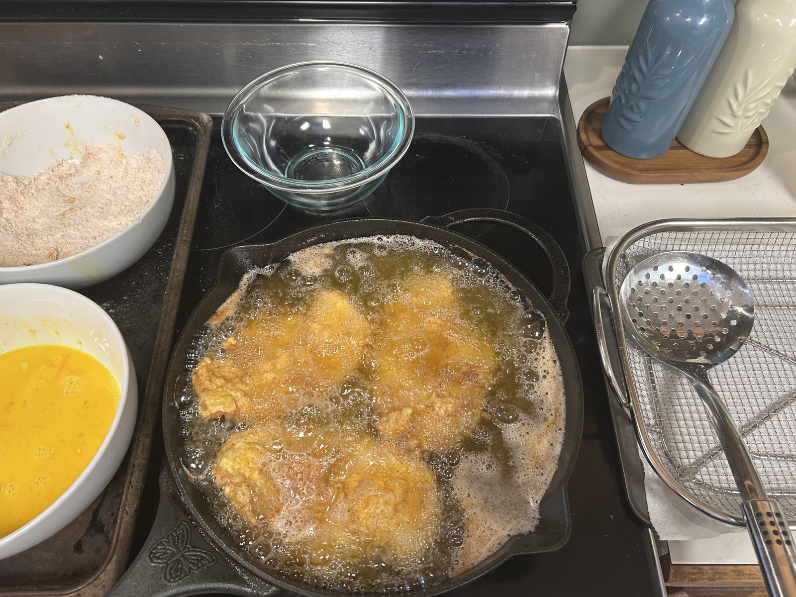 Chicken frying beside egg wash and seasoned flour for Nashville hot fried chicken sandwiches