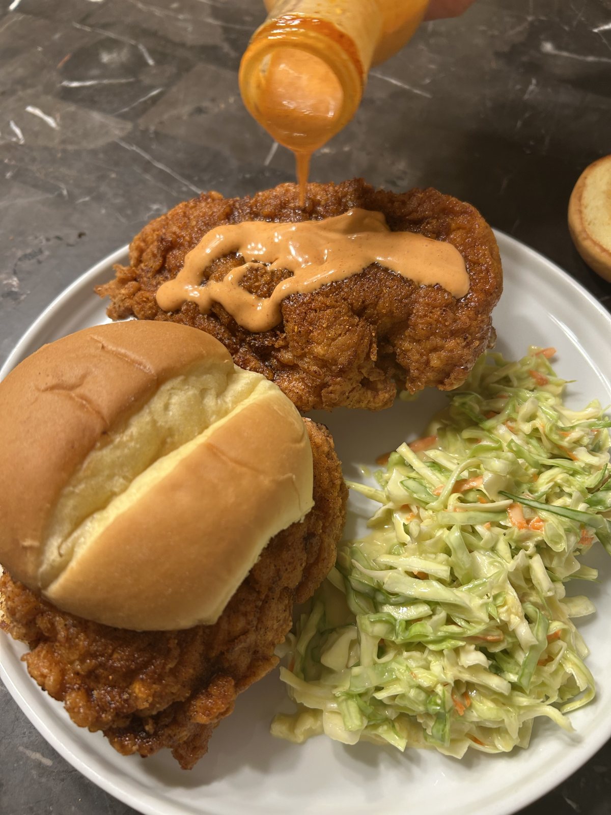 Hot seasoned oil being poured over fried chicken for a Nashville hot sandwich