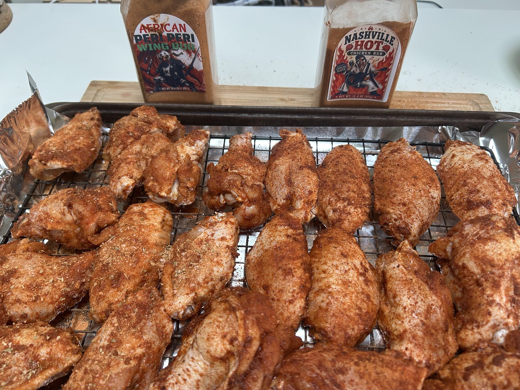 Chicken wings on a rack with African Peri Peri and Nashville Hot rub bottles