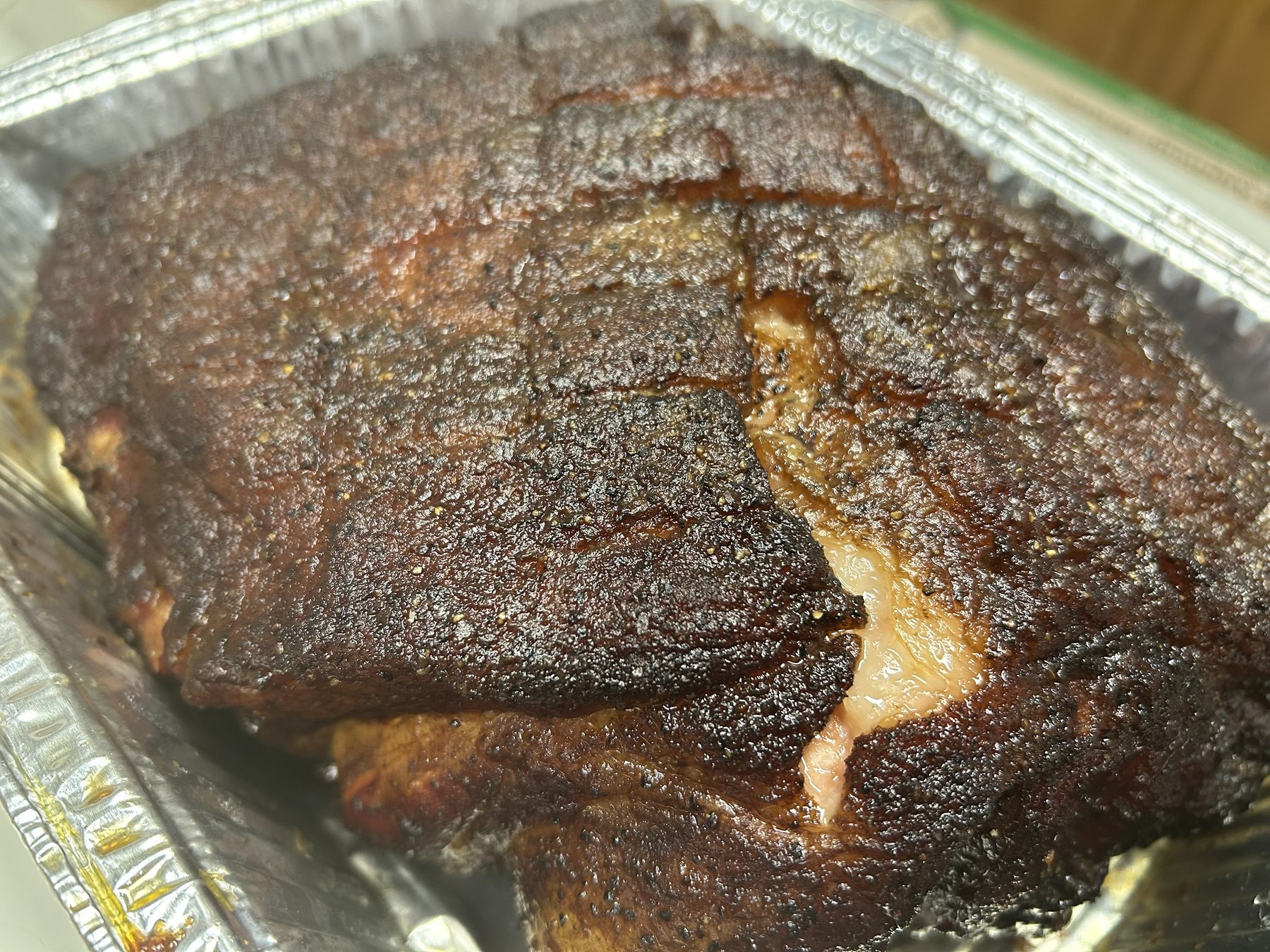 Smoked pork shoulder with dark bark resting in a foil pan