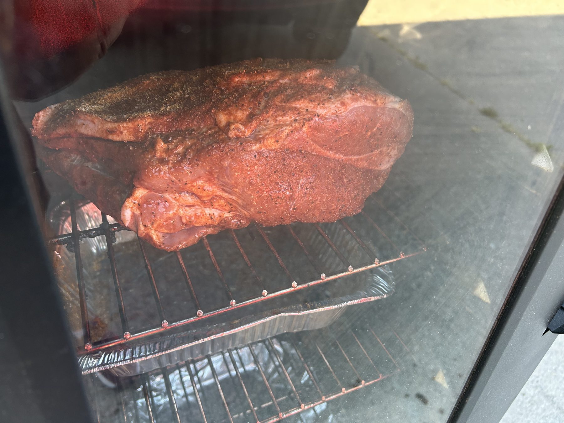 Pork shoulder coated in rub smoking on the upper rack