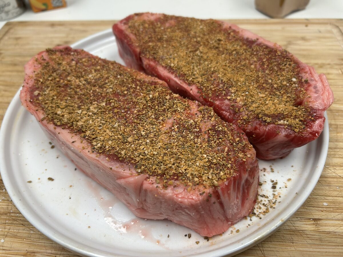 Two strip steaks coated in a brown Texas Beef Dust rub before cooking